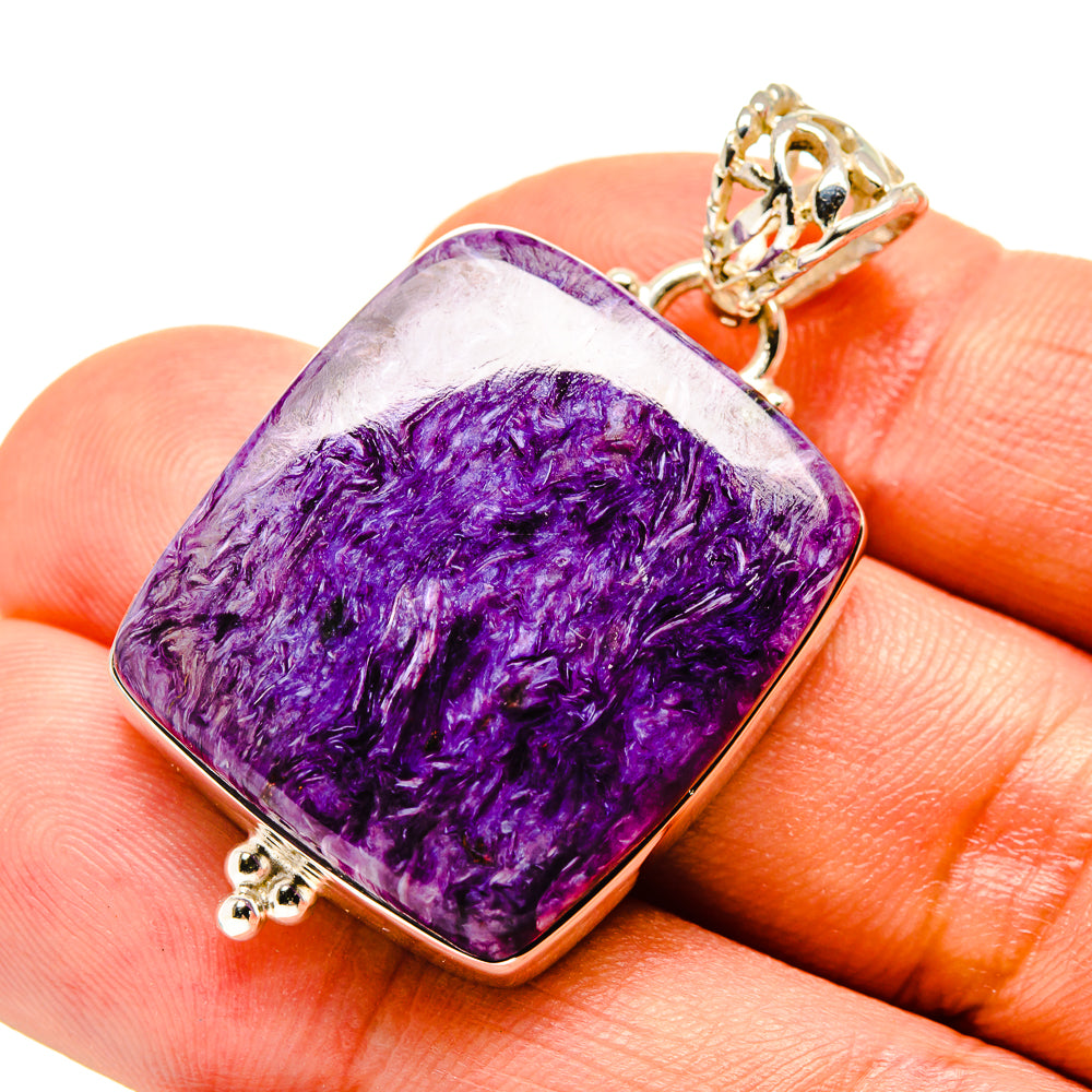 Charoite pendant with purple cushion-cut stone, gold-tone bail, held on fingertip