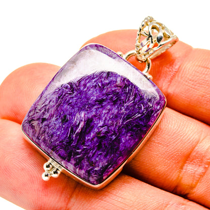 Charoite pendant with purple cushion-cut stone, gold-tone bail, held on fingertip