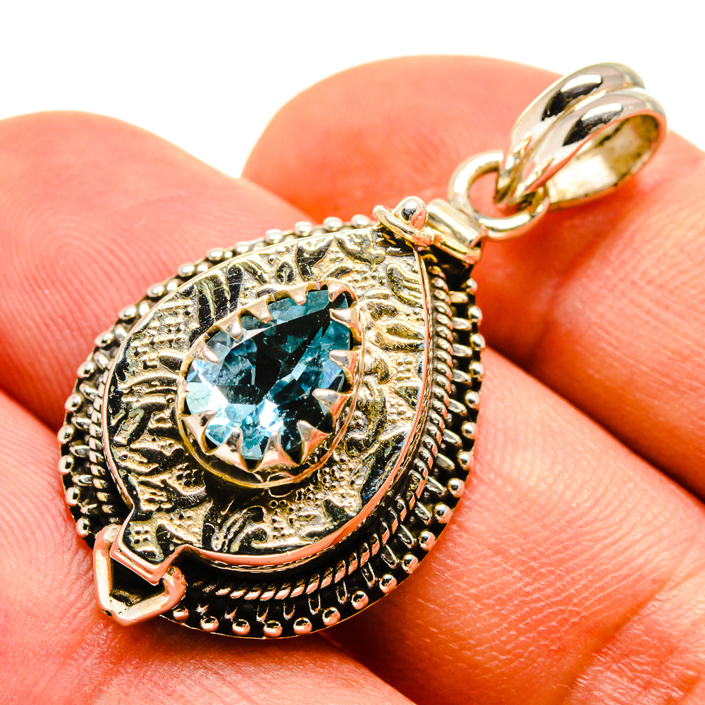 Ornate silver-tone pendant with blue gem teardrop bezel and loop bail on finger