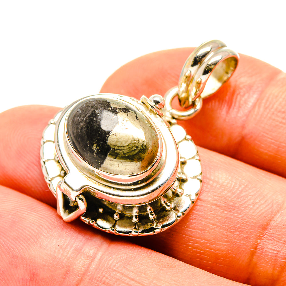 Black onyx oval pendant with ornate gold-tone frame and bail, on fingertip, 925 silver