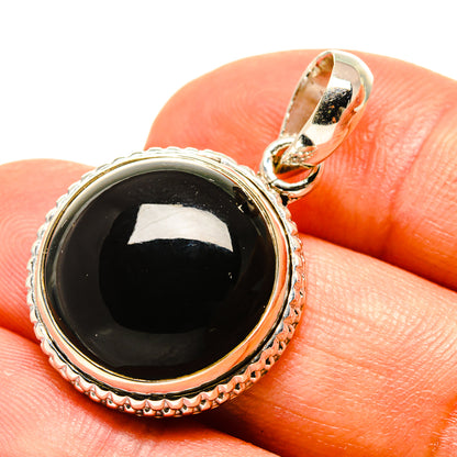 Round black onyx pendant in silver setting with bail, close on finger
