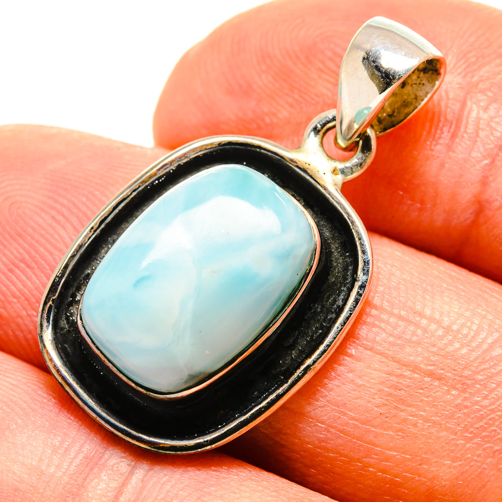 Larimar oval pendant on finger, black bezel with silver-toned bail and frame