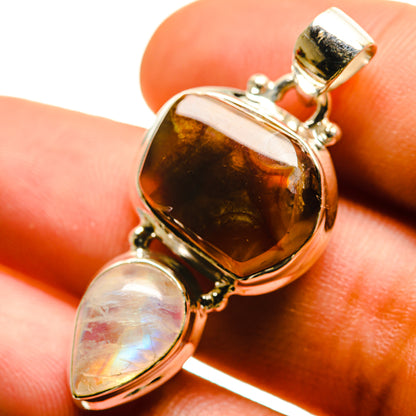 Sterling silver pendant on finger, showing amber fire agate oval and pale moonstone