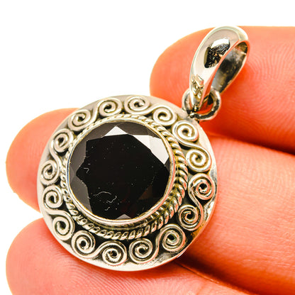 Round sterling silver pendant with ornate scroll frame and dark faceted gemstone