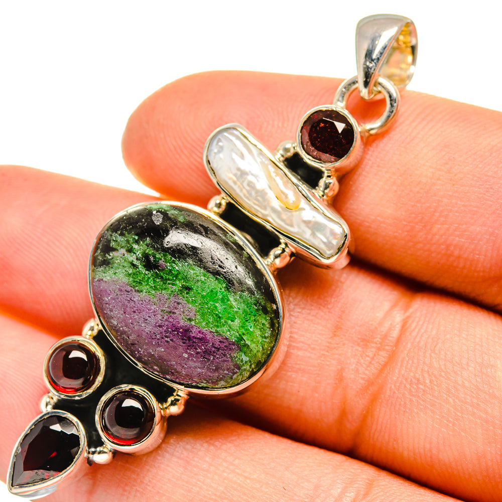 Gemstone pendant close-up on orange finger: oval green/purple stone, silver frame, red accents