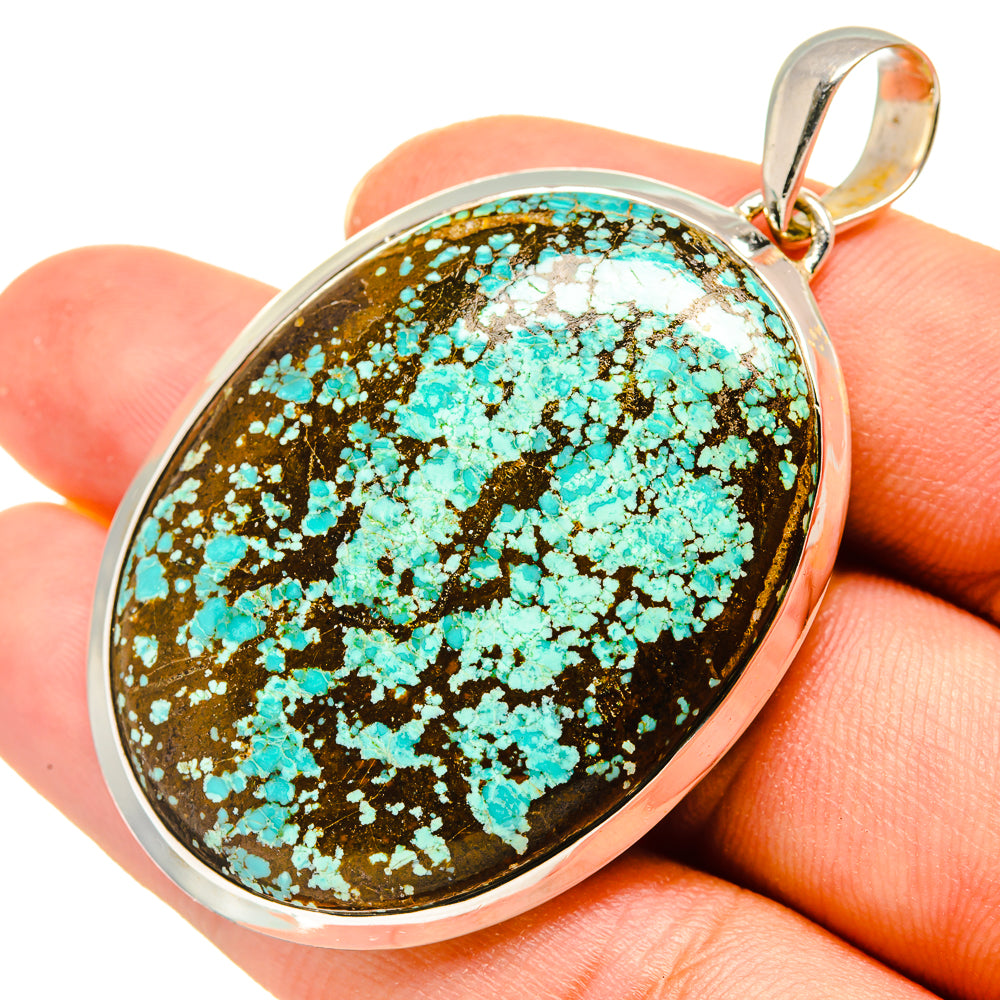 Oval turquoise pendant with speckled stone, sterling silver bail held in hand