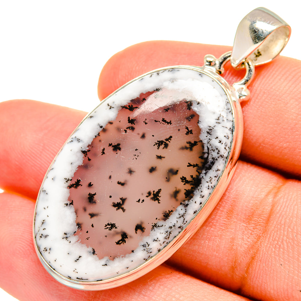Sterling silver oval dendritic opal pendant viewed on fingertip, polished bail