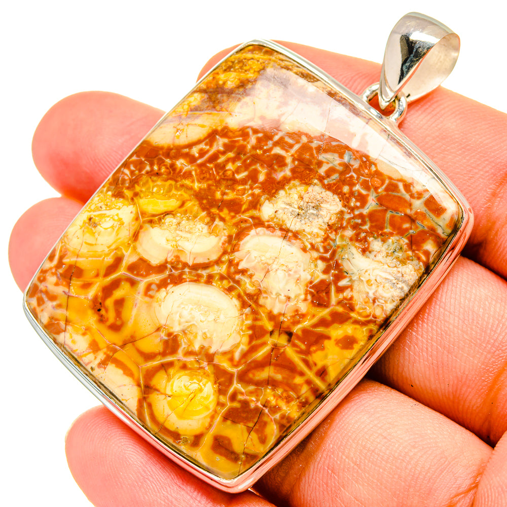 Amber-orange jasper pendant in silver frame, shown held in fingers