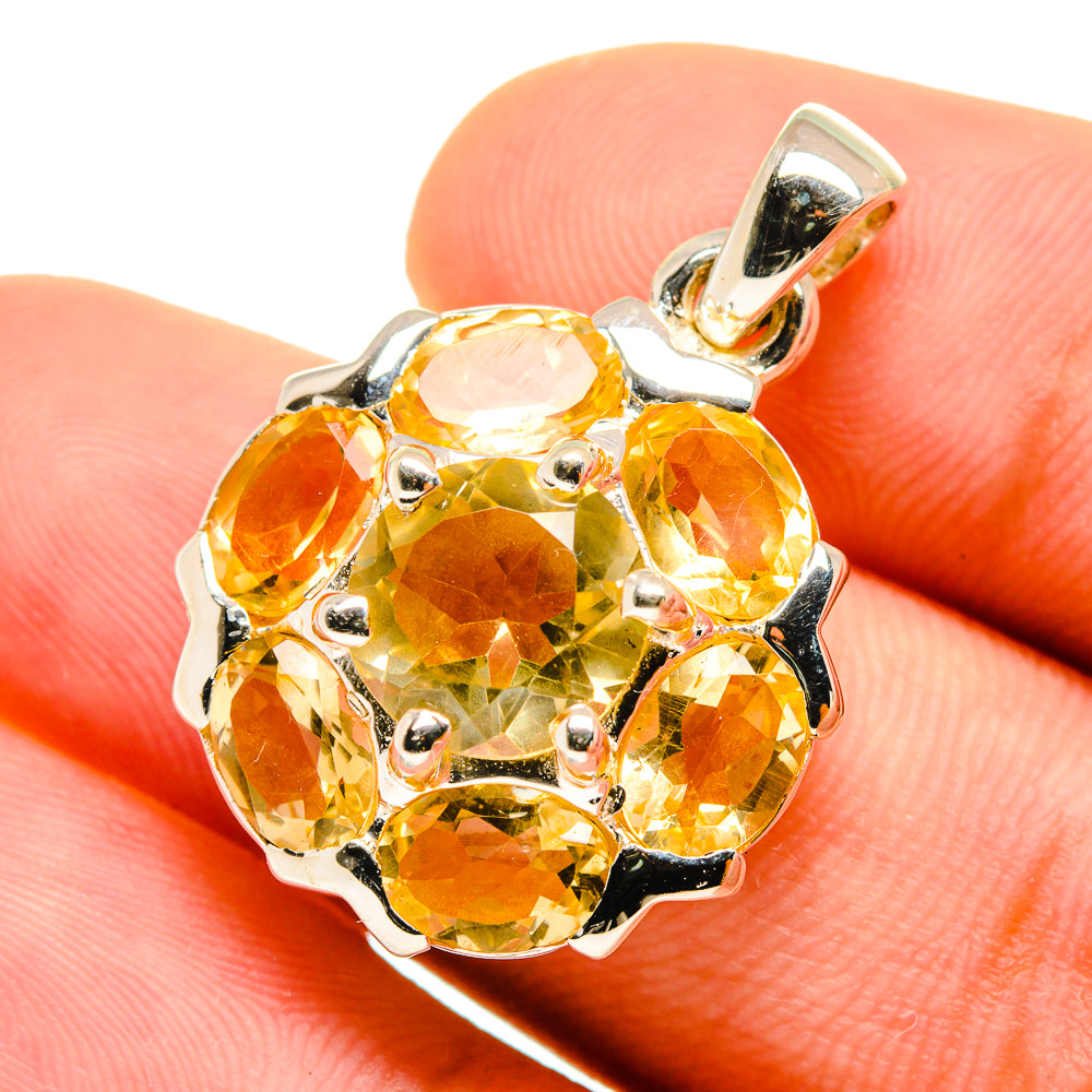 Faceted citrine pendant with yellow stones and silver bail, close-up on finger