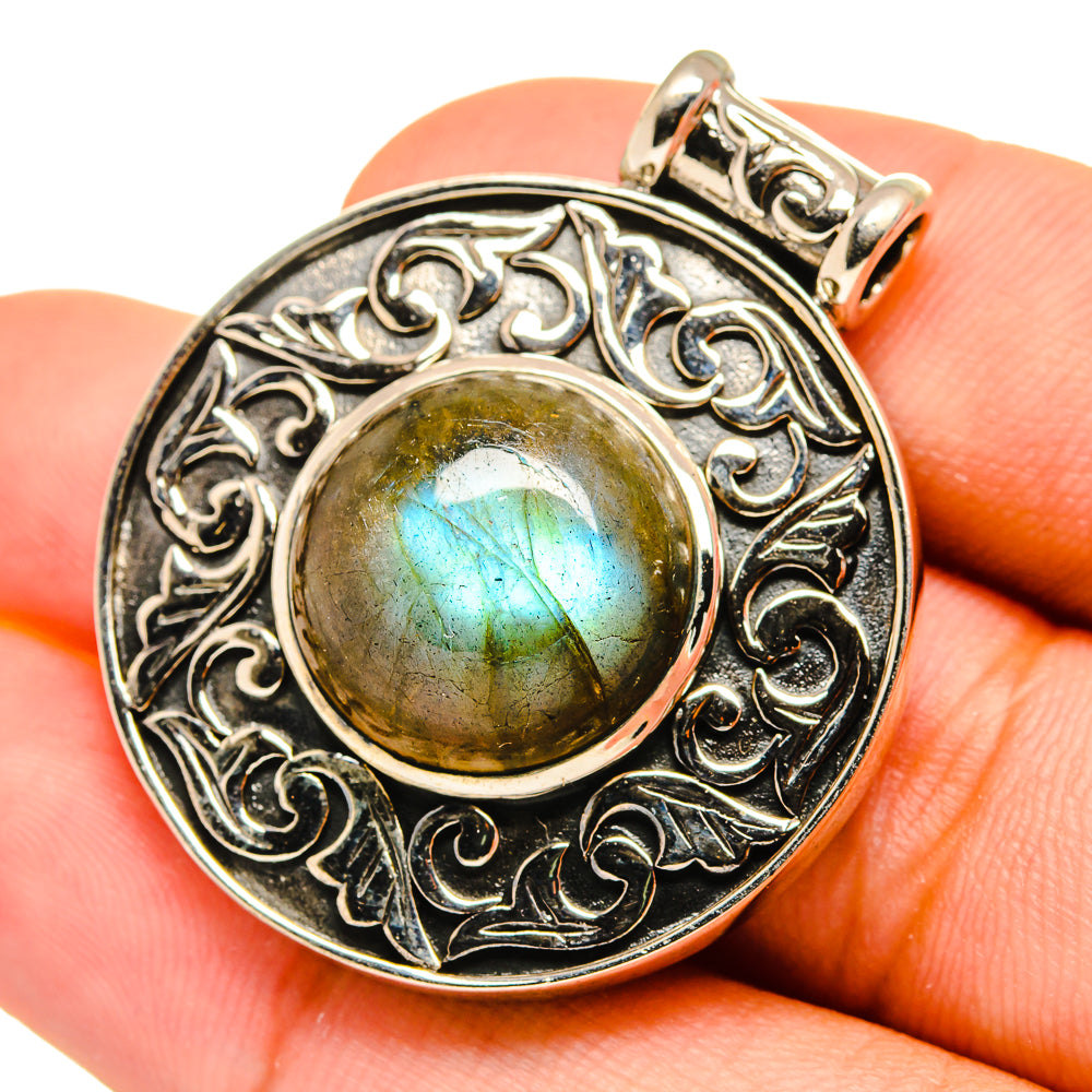 Labradorite pendant close-up on hand: round golden stone with blue flash in silver filigree