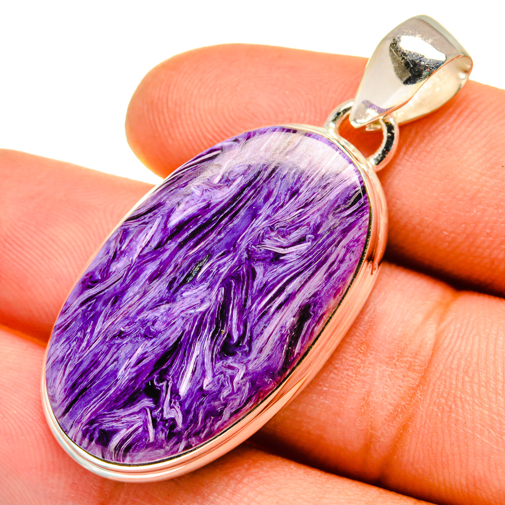Oval charoite pendant with purple veining, 925 silver bezel and bail; close-up on finger
