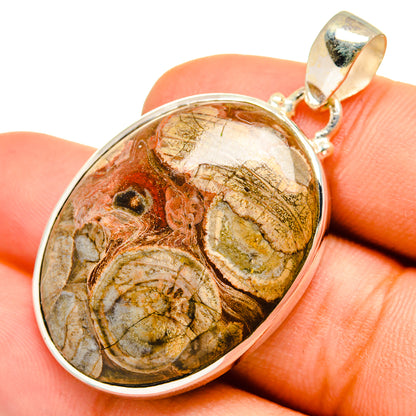 Mushroom rhyolite pendant, oval stone with gold-toned bail held in fingers