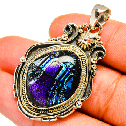 Sterling silver oval dichroic glass pendant, held on fingertip, blue-purple iridescent