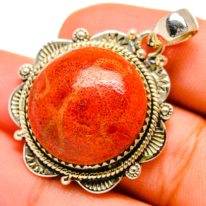 Sponge coral pendant with orange cabochon and sterling silver filigree, held in fingers