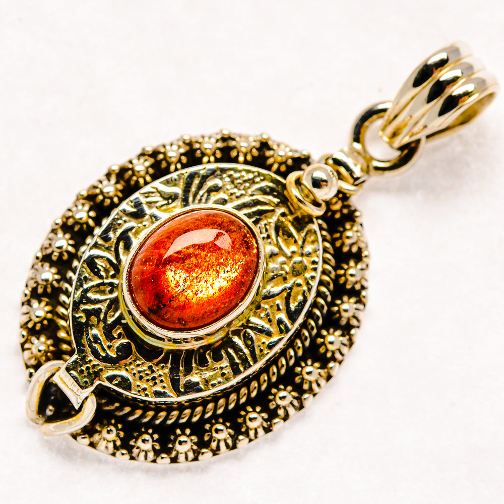 Round ornamental pendant with orange sunstone cabochon, detailed scalloped frame