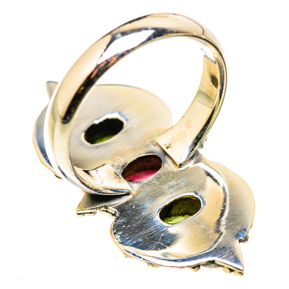 Sterling silver ring underside with cutout openwork and hints of green and pink gemstones.