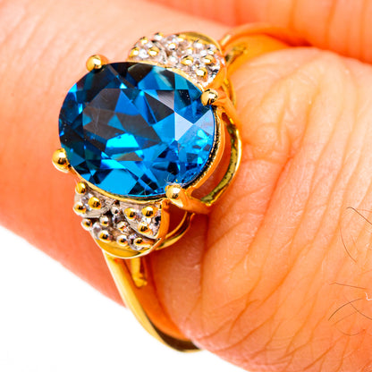 Gold oval blue gemstone ring with sparkling zircon halo and side accents, on finger