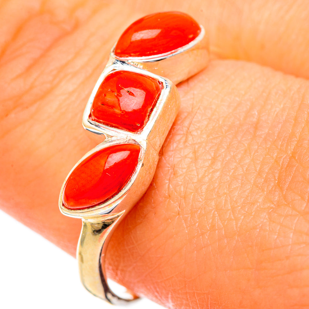 Red coral triple-stone ring on finger, oval stones in shiny metal bezel