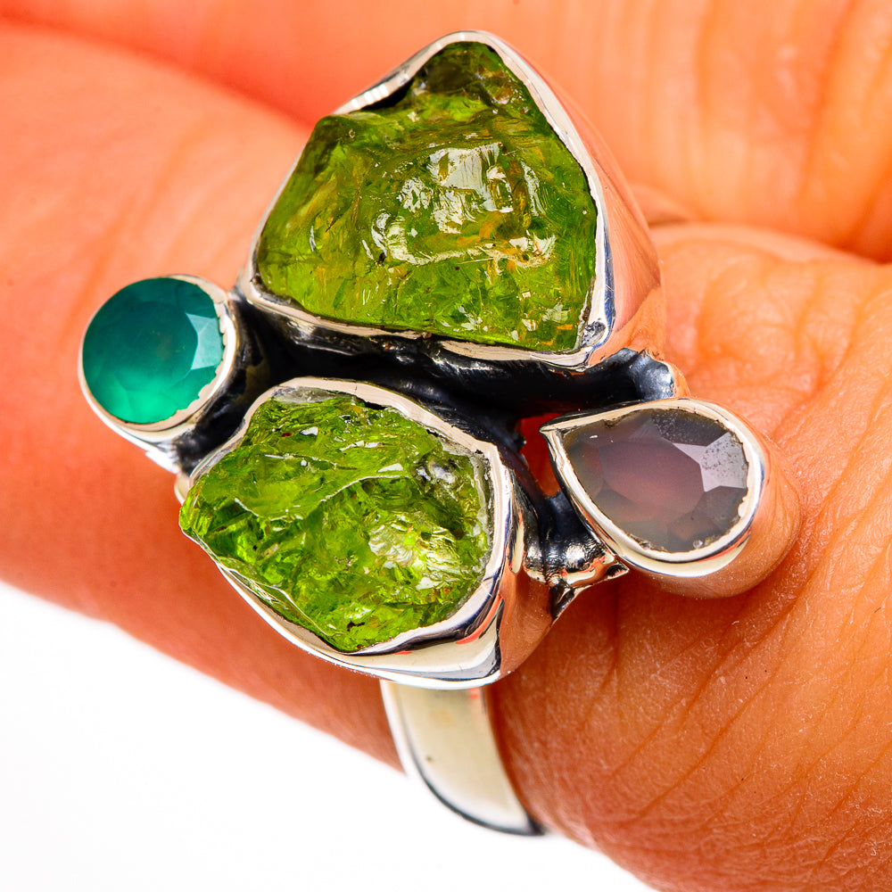 Green and teal gemstone cluster ring with dark metal prongs; close-up on finger