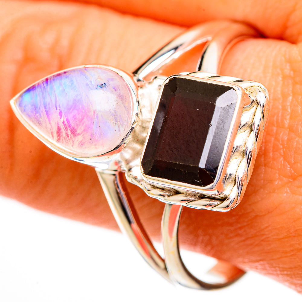 Silver-tone ring close-up: oval pink moonstone with square dark red garnet in pronged setting