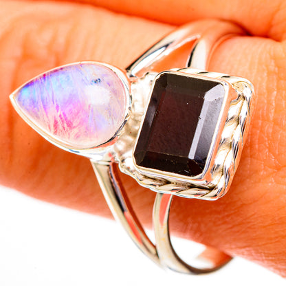 Silver-tone ring close-up: oval pink moonstone with square dark red garnet in pronged setting