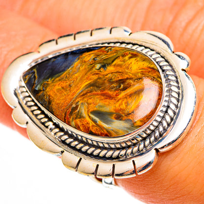 Oval pietersite cabochon ring on finger, silver twisted-edge bezel with orange-gold stone