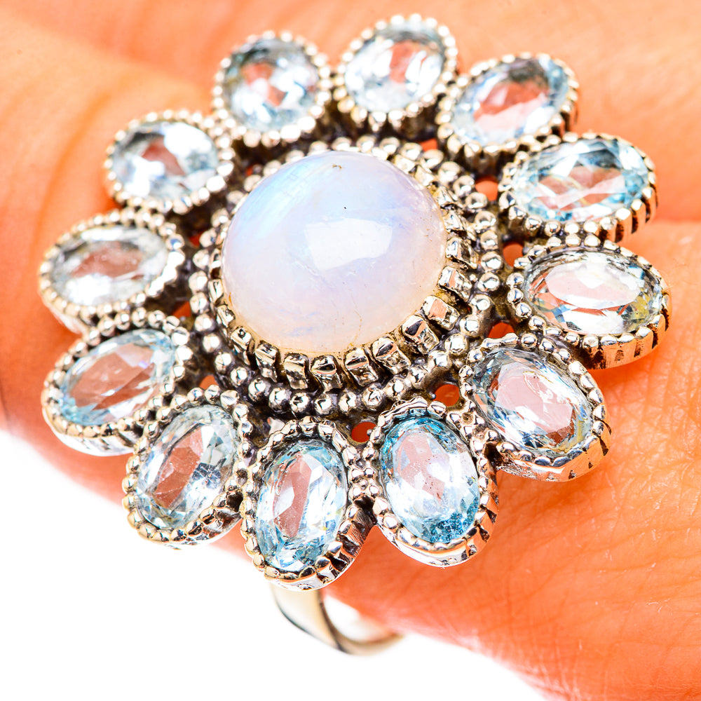 Oval opal-like center ring surrounded by blue stones, ornate silver prong setting on finger