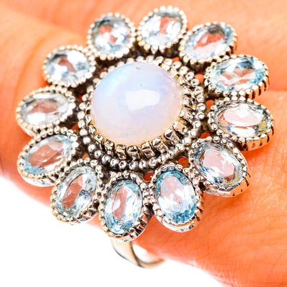 Oval opal-like center ring surrounded by blue stones, ornate silver prong setting on finger