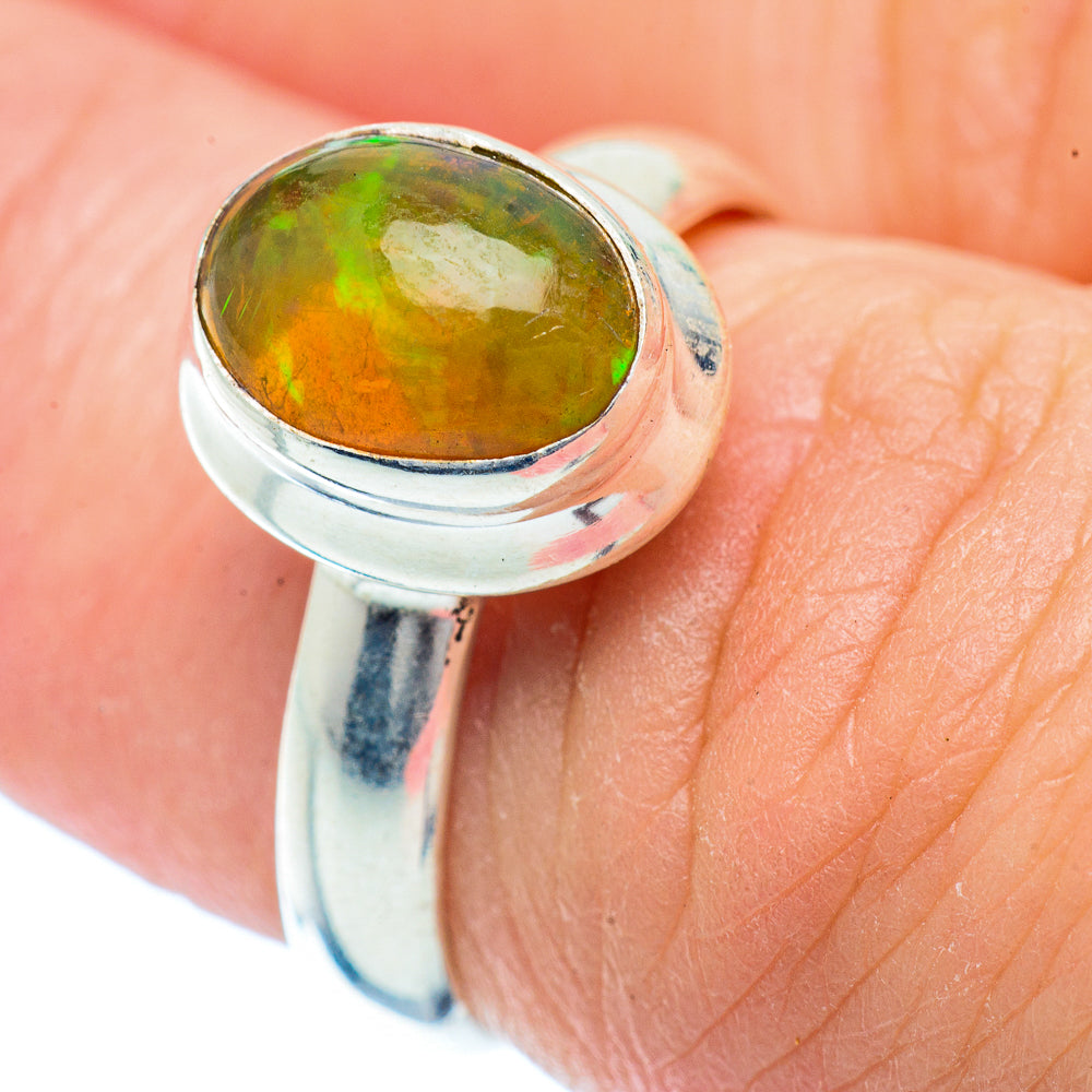 Sterling silver ring with oval green-orange opal cabochon on finger, bezel set