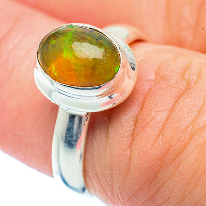 Sterling silver ring with oval green-orange opal cabochon on finger, bezel set