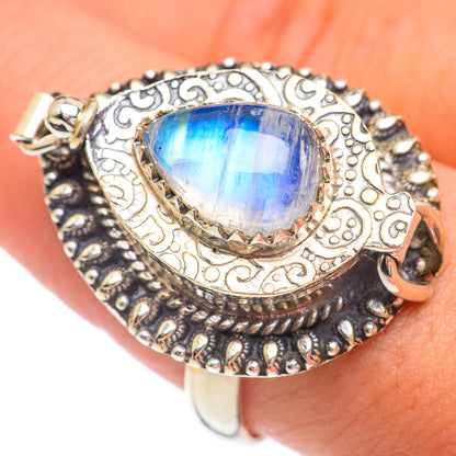 Teardrop blue moonstone poison ring with ornate gold-tone filigree, worn on finger
