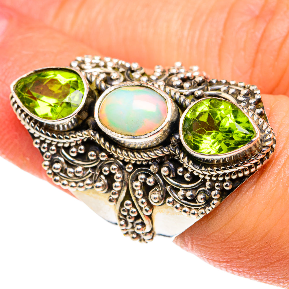 Silver ring on finger with green round peridot stones and central opal cabochon.