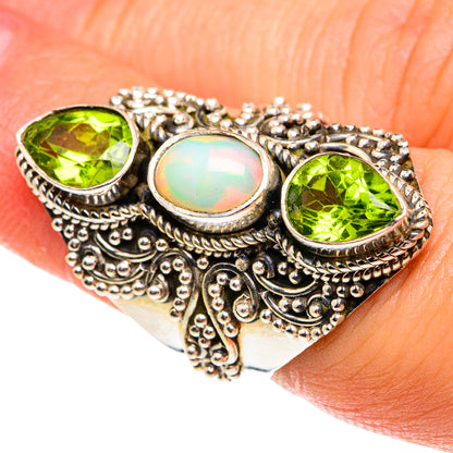 Silver ring on finger with green round peridot stones and central opal cabochon.