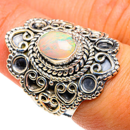 Sterling silver opal ring on finger, round iridescent cabochon with detailed scrollwork