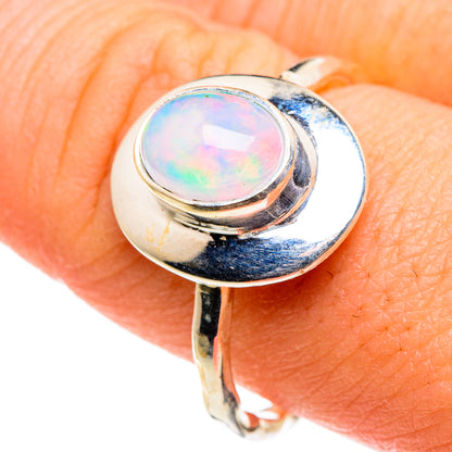 Oval iridescent opal set in polished silver ring, shown on finger