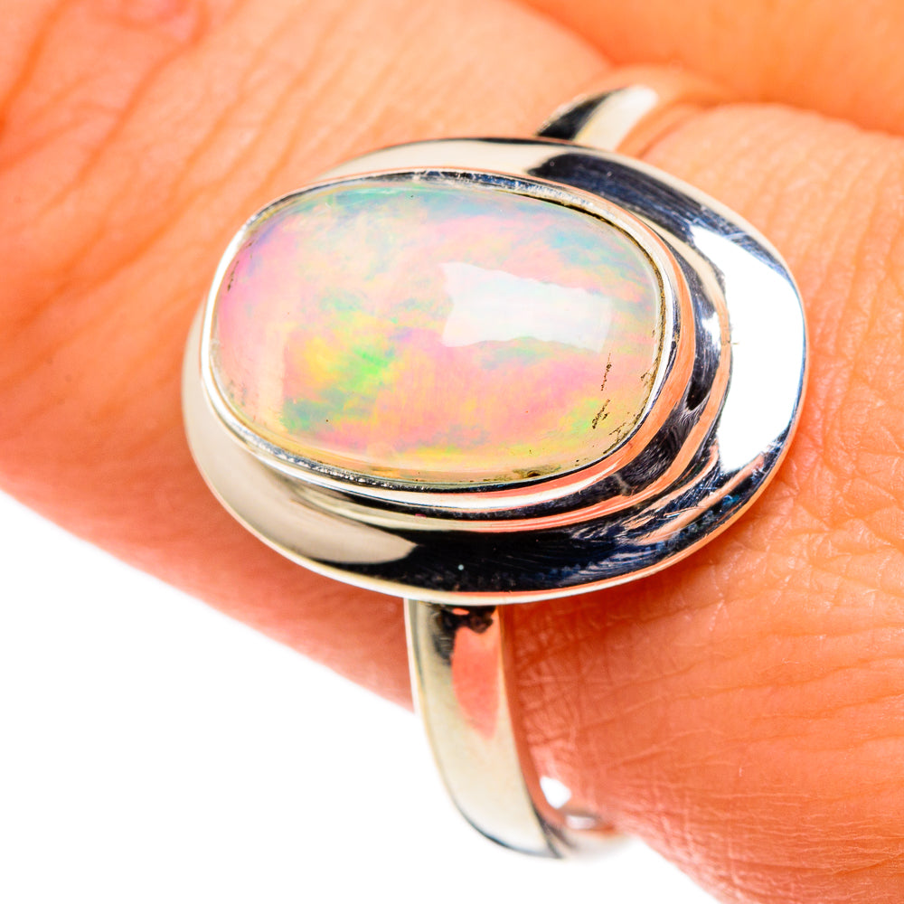 Oval opal cabochon ring in bright silver with dark setting, shown on finger
