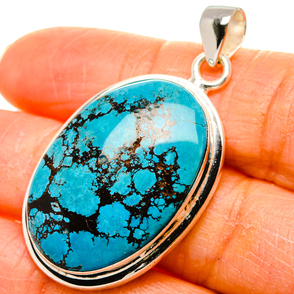 Oval turquoise pendant with black matrix, sterling silver bail, close-up on gemstone.